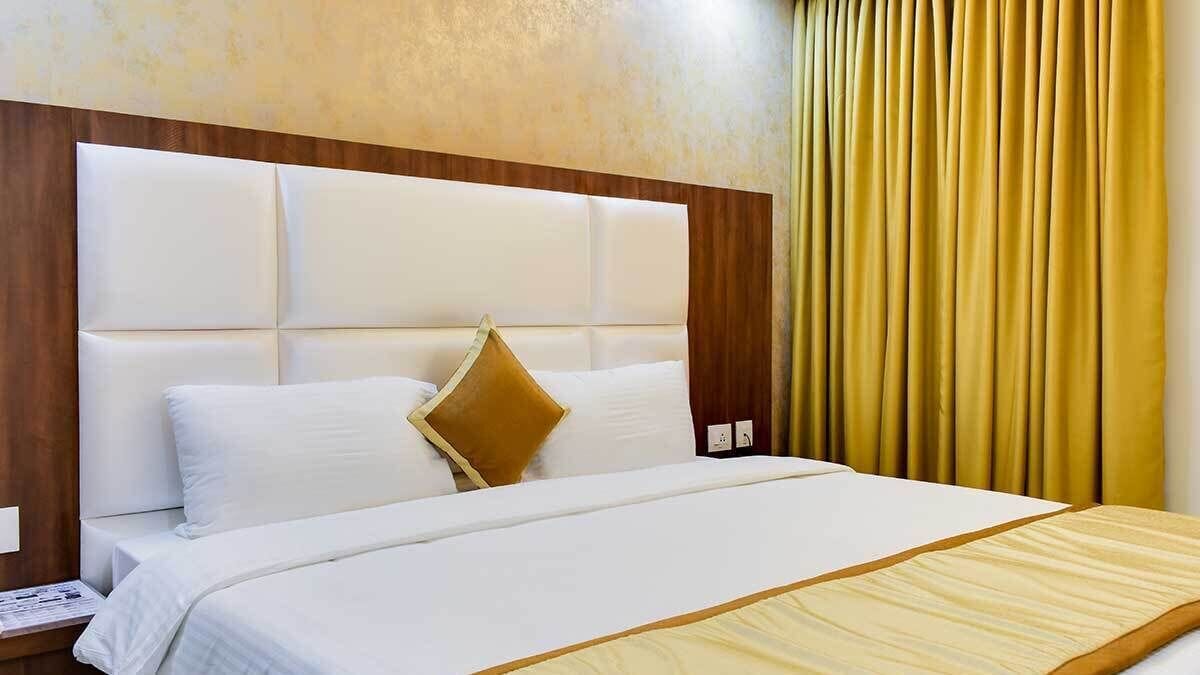 A hotel room with a large bed, a wooden headboard, and a yellow curtain.