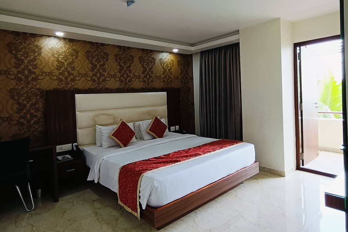 A spacious bedroom with a large bed, a nightstand, a desk, and a view of the outdoors.