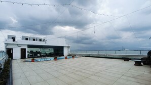 Una terraza en la azotea con piscina, zona de estar y un edificio moderno con grandes ventanales.
