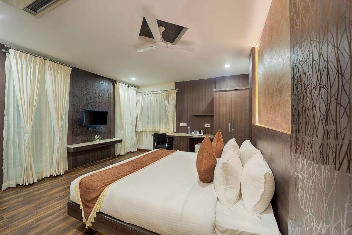 A hotel room with a large bed, a desk, a TV, and a ceiling fan.
