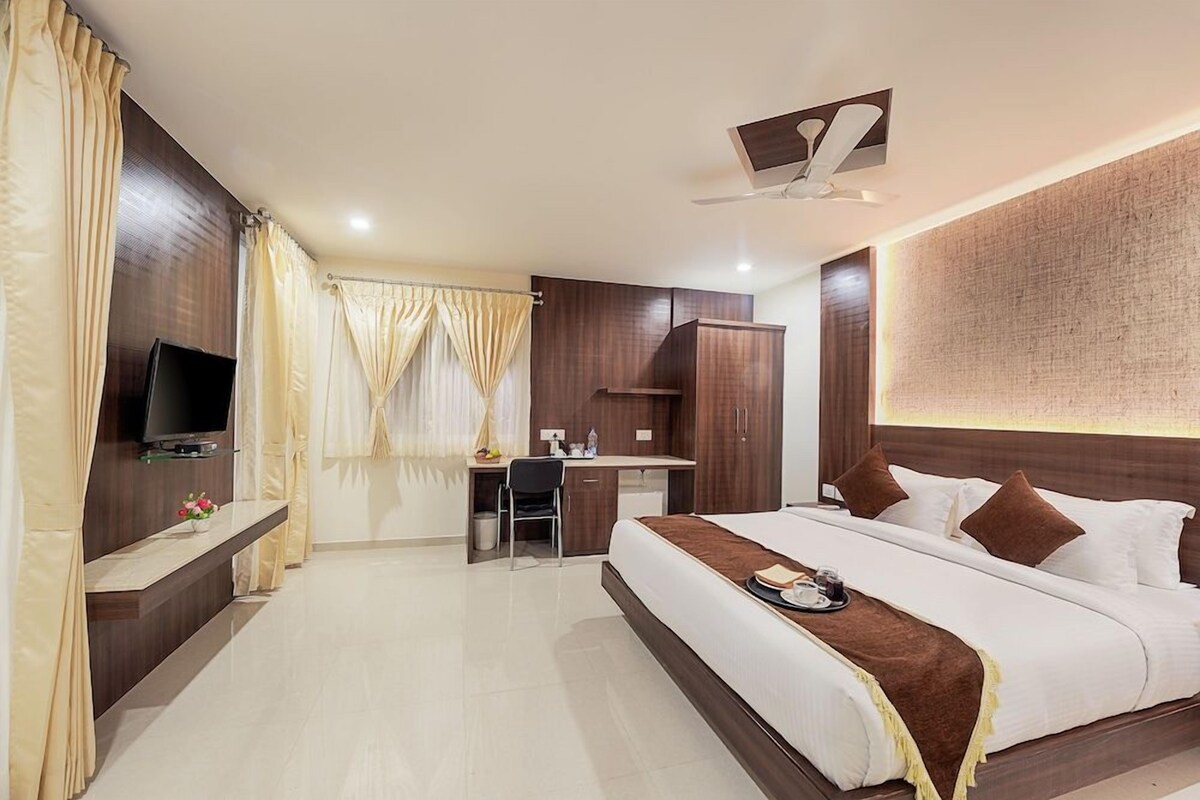 Une chambre d’hôtel avec un lit, un bureau, une télévision et une grande fenêtre avec des rideaux.