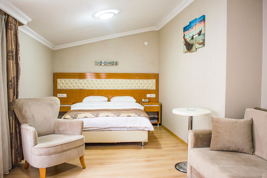 Een hotelkamer met een groot bed, twee fauteuils, een klein rond tafeltje en een schilderij aan de muur.