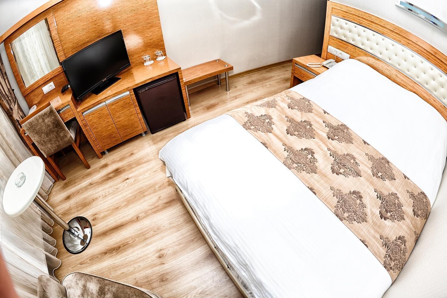 Hotelkamer met een bed, een televisie, een bureau met een computer, een kleine koelkast en een nachtkastje met een lamp.