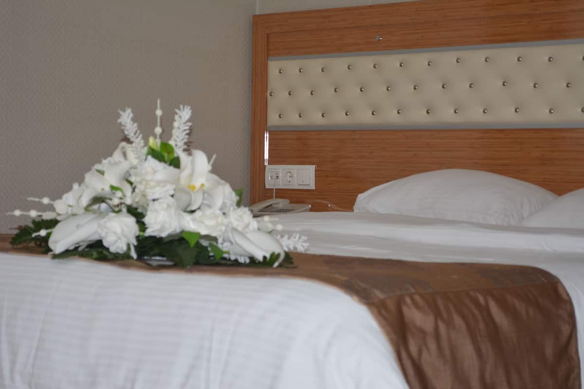 Ein Hotelzimmer mit einem hölzernen Kopfteil, einem Bett mit weißer Bettwäsche und einer Blumenkomposition auf dem Bett.