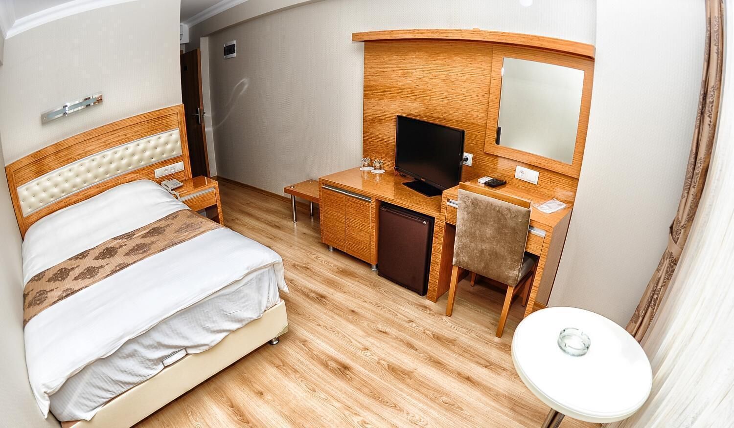 Ett hotellrum med en säng, ett skrivbord med en tv, en spegel och ett litet runt bord.