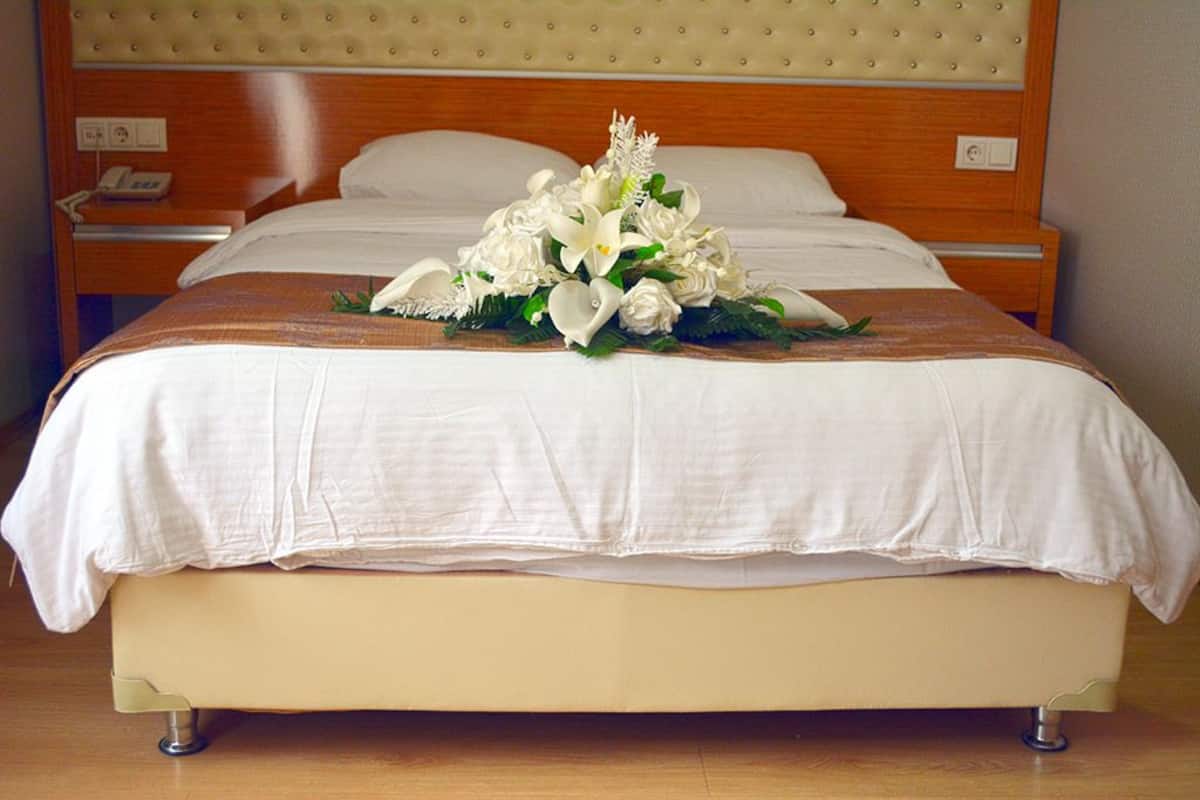 Ein Hotelzimmer mit einem Bett, einem Holz-Kopfteil, einem Nachttisch mit Telefon und einer Blumenkomposition auf dem Bett.