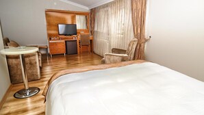 Une chambre d’hôtel avec un grand lit, une petite table ronde, un canapé, une télévision et un mini-bar.