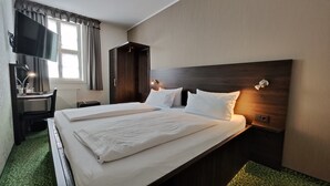 A hotel room with a large bed, a desk with a chair, a TV, and a wardrobe. - Hotel Alte Brennerei (Wernigerode)