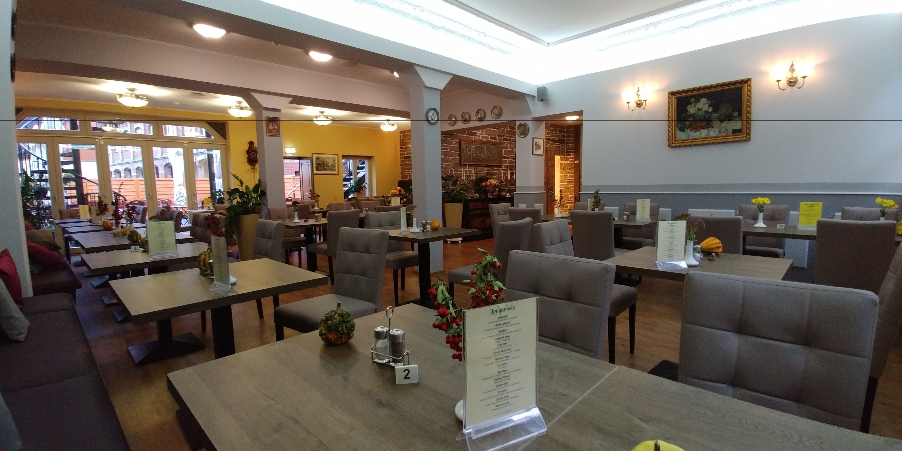 Un restaurante con varias zonas de estar, incluidas cabinas y mesas. Se muestran menús en soportes, y el interior combina elementos de ladrillo y madera.