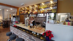 A bar area with a bartender, shelves of various liquor bottles, a stone counter, and bar stools. - Hotel Alte Brennerei (Wernigerode)