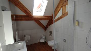 Ein Badezimmer mit Oberlicht, Holzbalken, einer Dusche und einem WC.