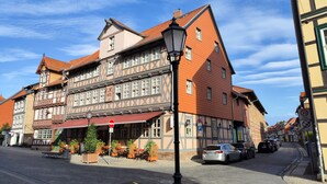 A traditional half-timbered building with a red awning, a sign for 'Hotel', and outdoor seating with plants. - Hotel Alte Brennerei (Wernigerode)