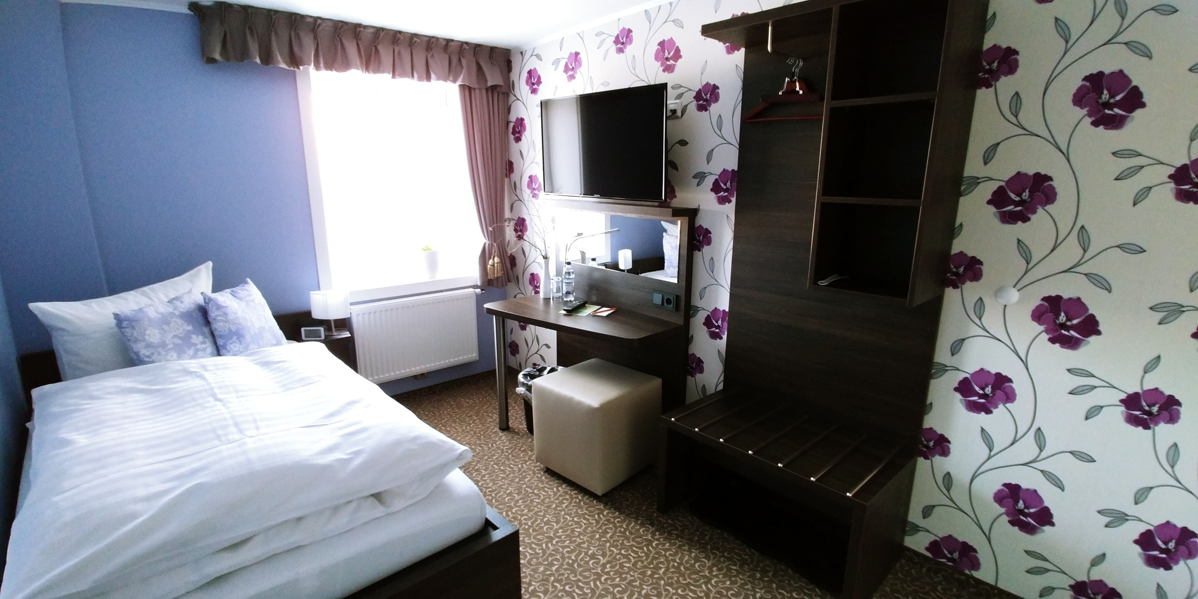 A hotel room with a bed, a desk, a television, and a wardrobe.