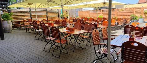 An outdoor café with wooden tables and chairs, numbered seating, and yellow umbrellas.