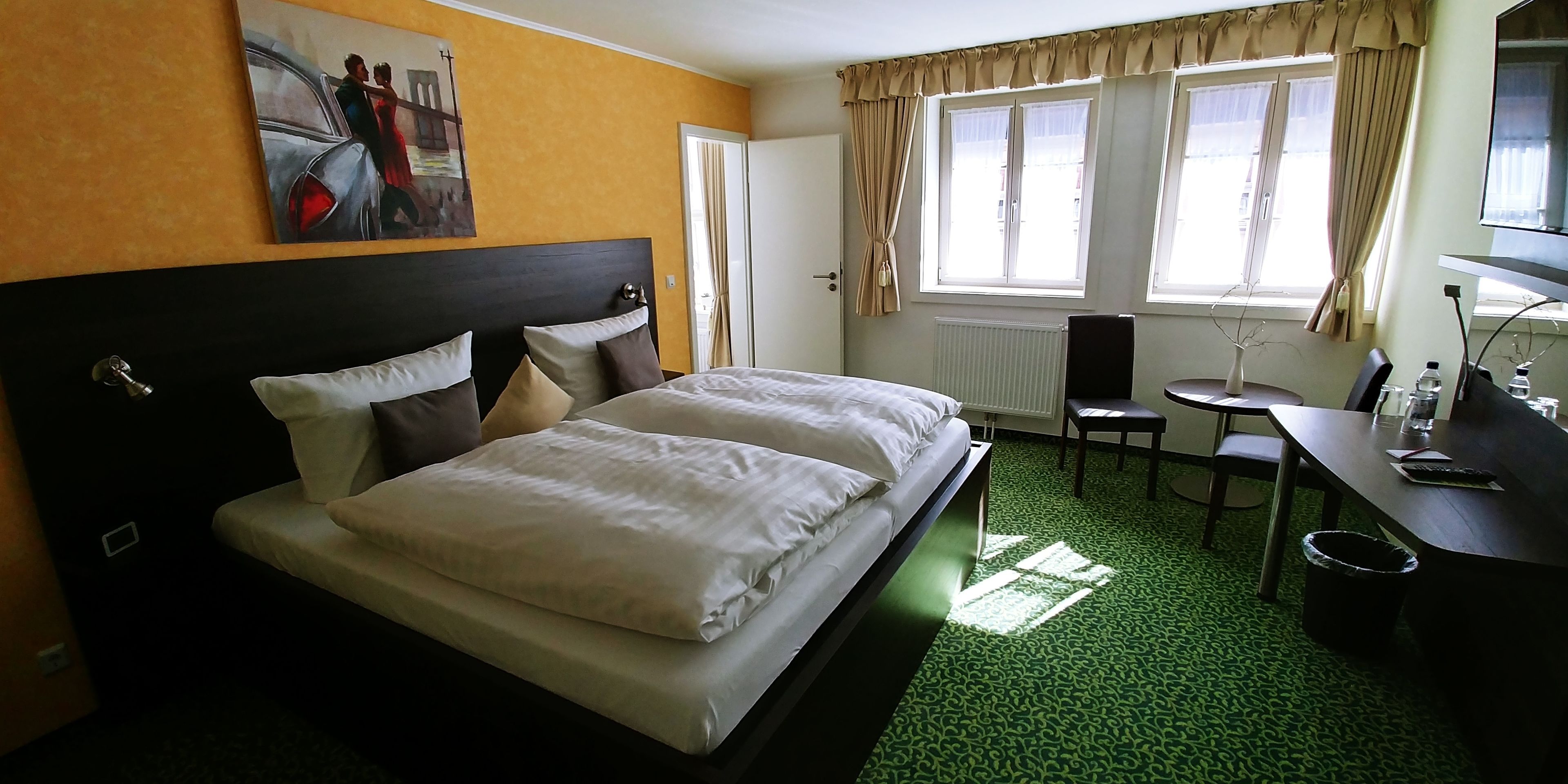 Une chambre d’hôtel avec un grand lit, un bureau, une chaise, un radiateur et une fenêtre avec des rideaux.