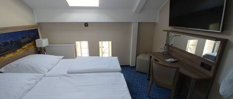 A hotel room with a large bed, a desk, a television, and a window.