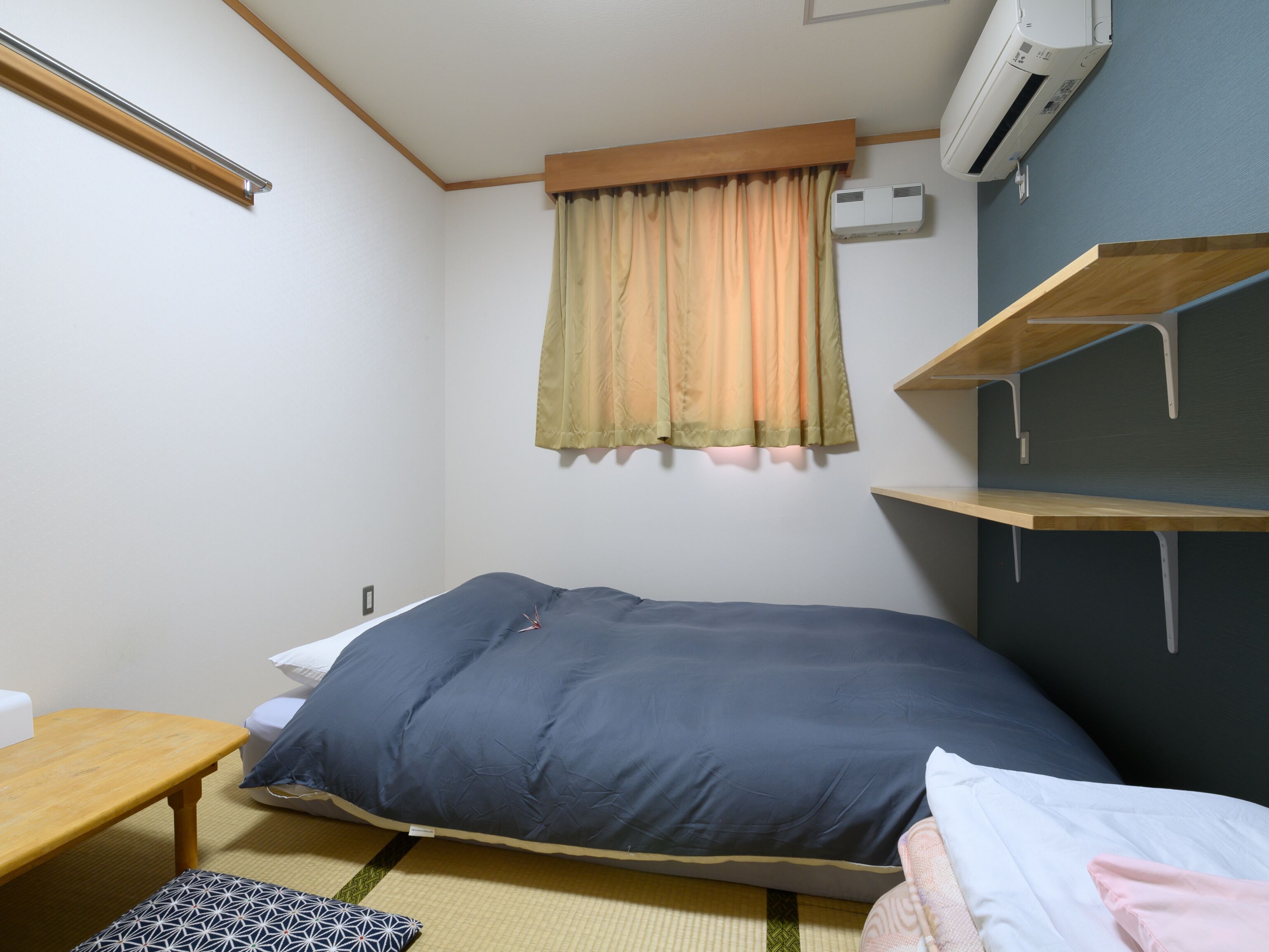 Una camera da letto piccola e ordinata con un letto singolo, un comodino, una scaffalatura e una finestra con tende.
