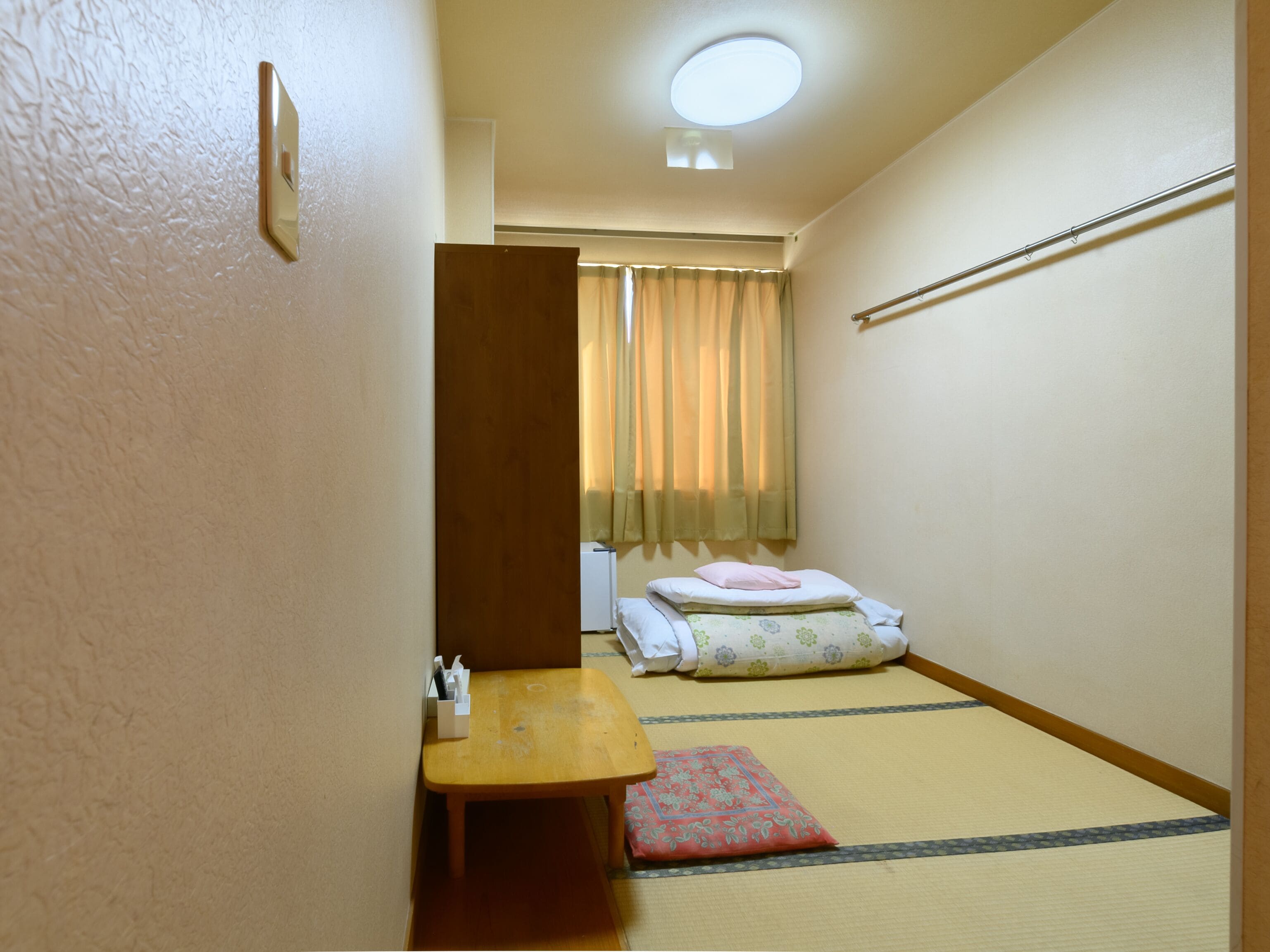 A traditional Japanese room with tatami flooring, a low wooden table, a bed with a floral-patterned mattress, and a sliding door.