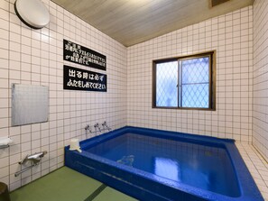 Kylpyhuone, jossa on suuri kylpyamme, ikkuna ja laatoitetut seinät.