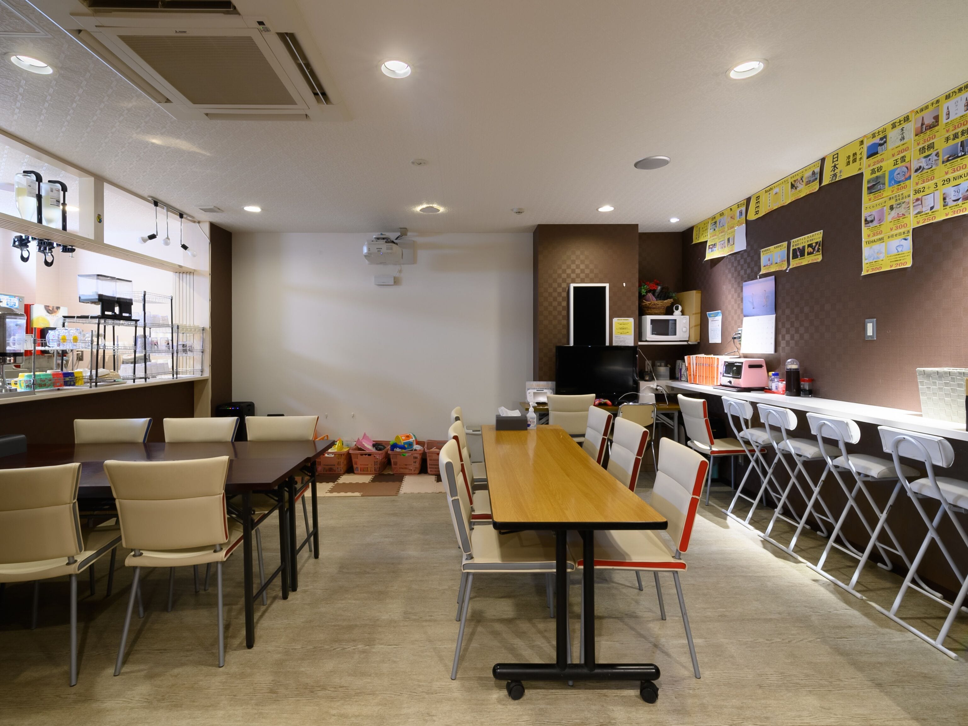 A restaurant with a long wooden table and chairs, a counter with a display of food items, and a wall with hanging signs.
