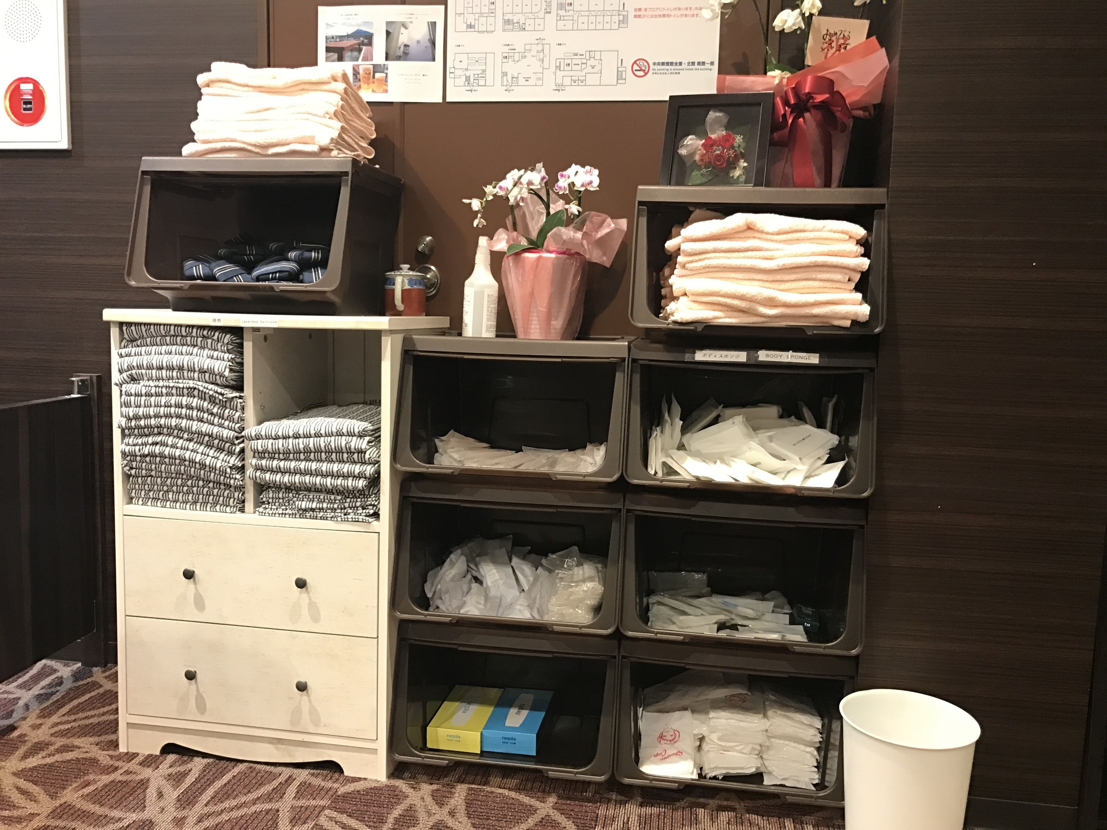 Habitación de hotel con un armario ordenado que contiene toallas, artículos de aseo y un florero con flores.