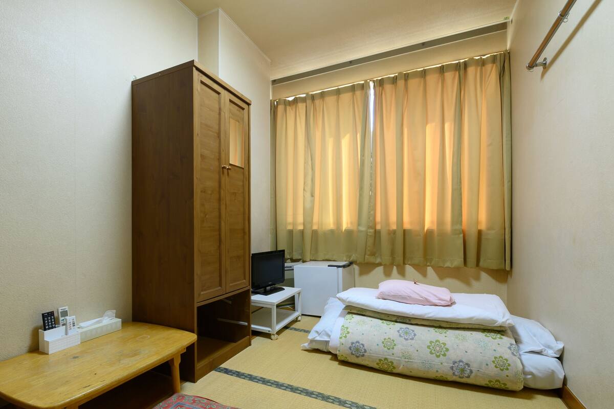 A small room with a bed, a desk, a wardrobe, and a window with curtains.