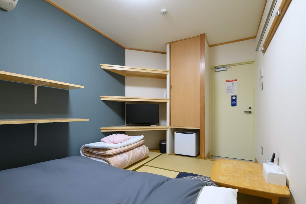 A compact hotel room with a bed, a desk, and built-in shelves.