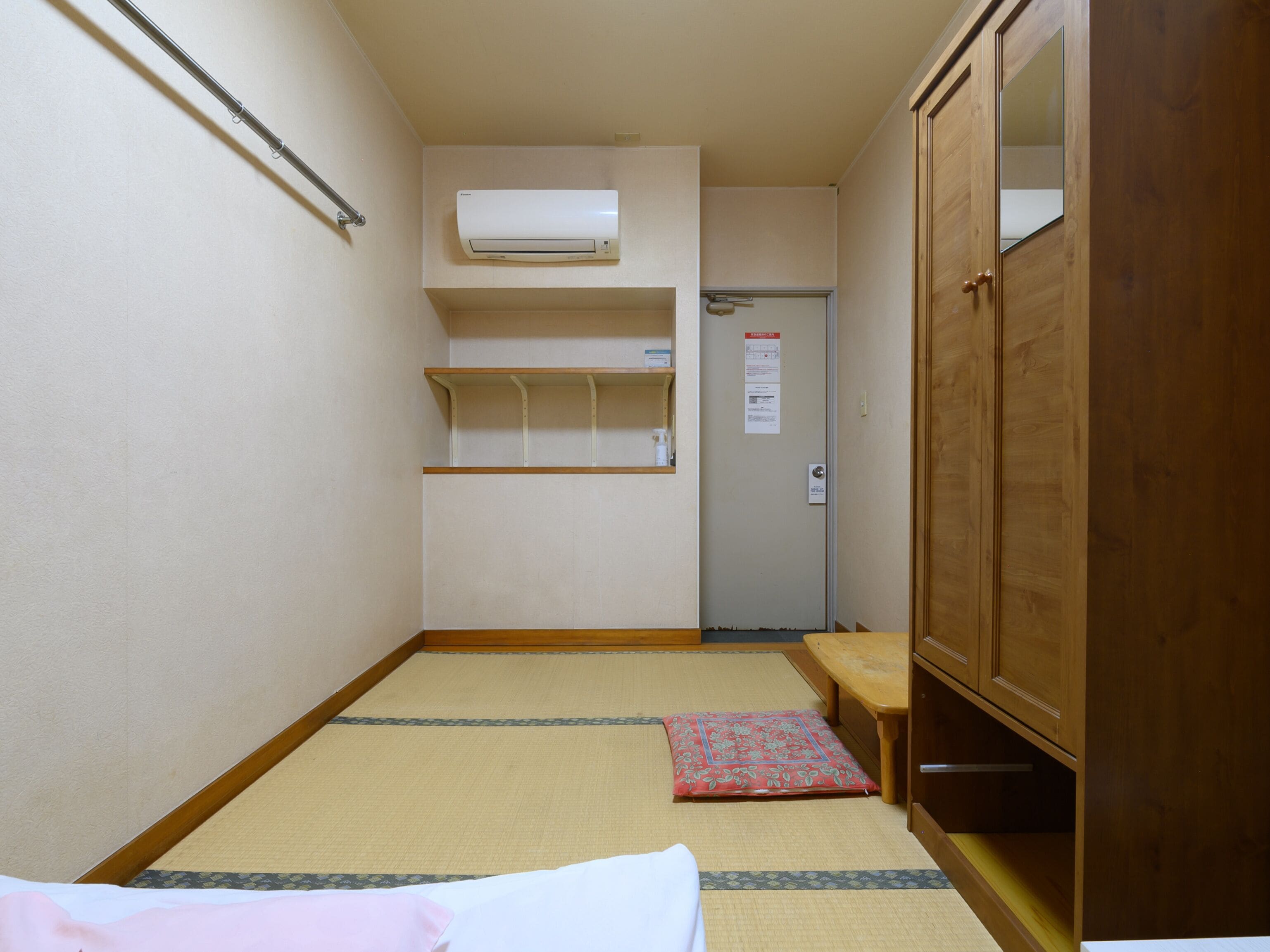 Habitación de hotel estrecha con suelo de tatami, un armario de madera, una mesita y una estantería.