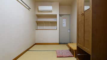 Habitación de hotel estrecha con suelo de tatami, un armario de madera, una mesita y una estantería.