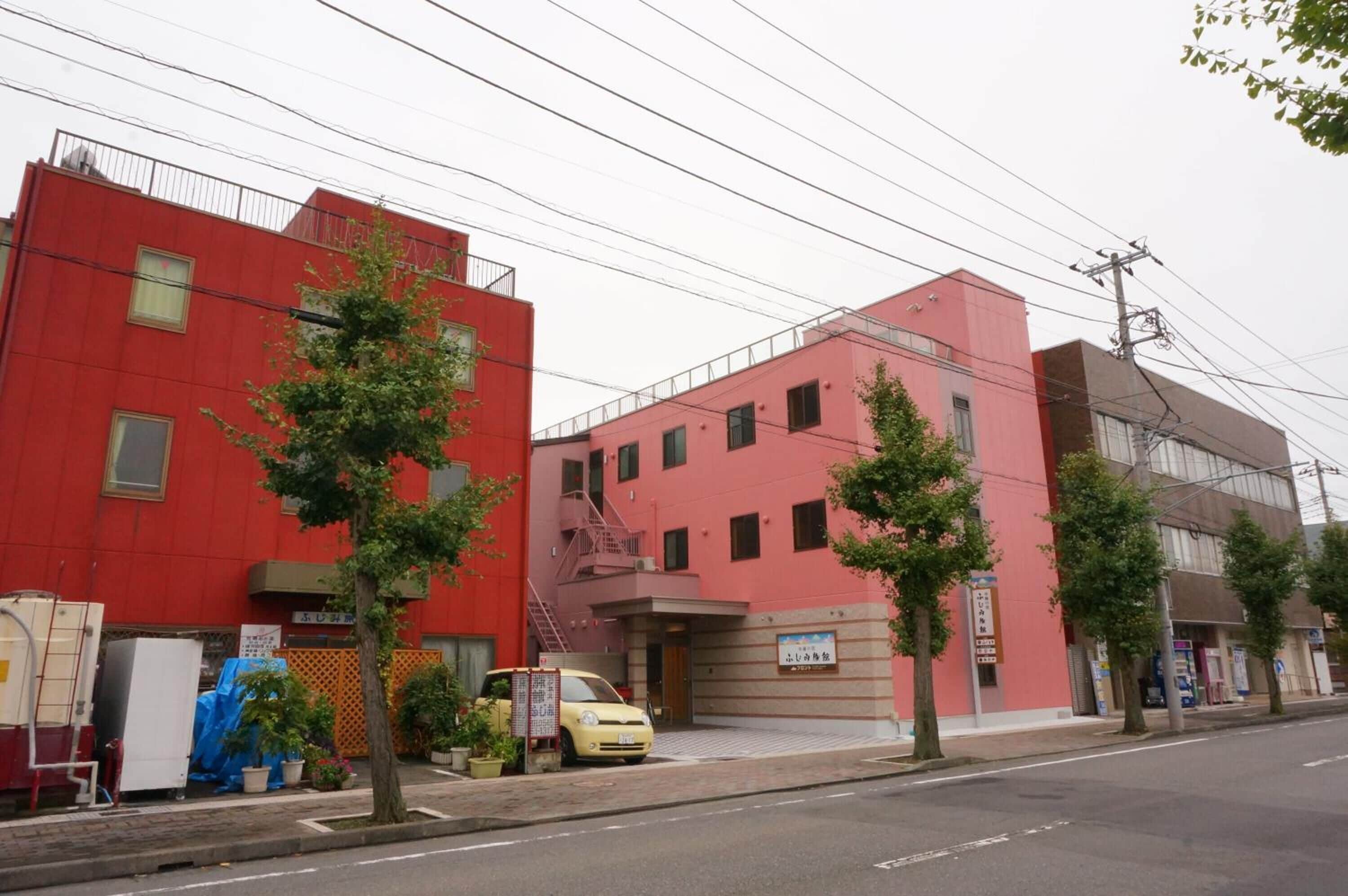 A red building with a fire escape, a yellow car parked in front, and several trees along the sidewalk.