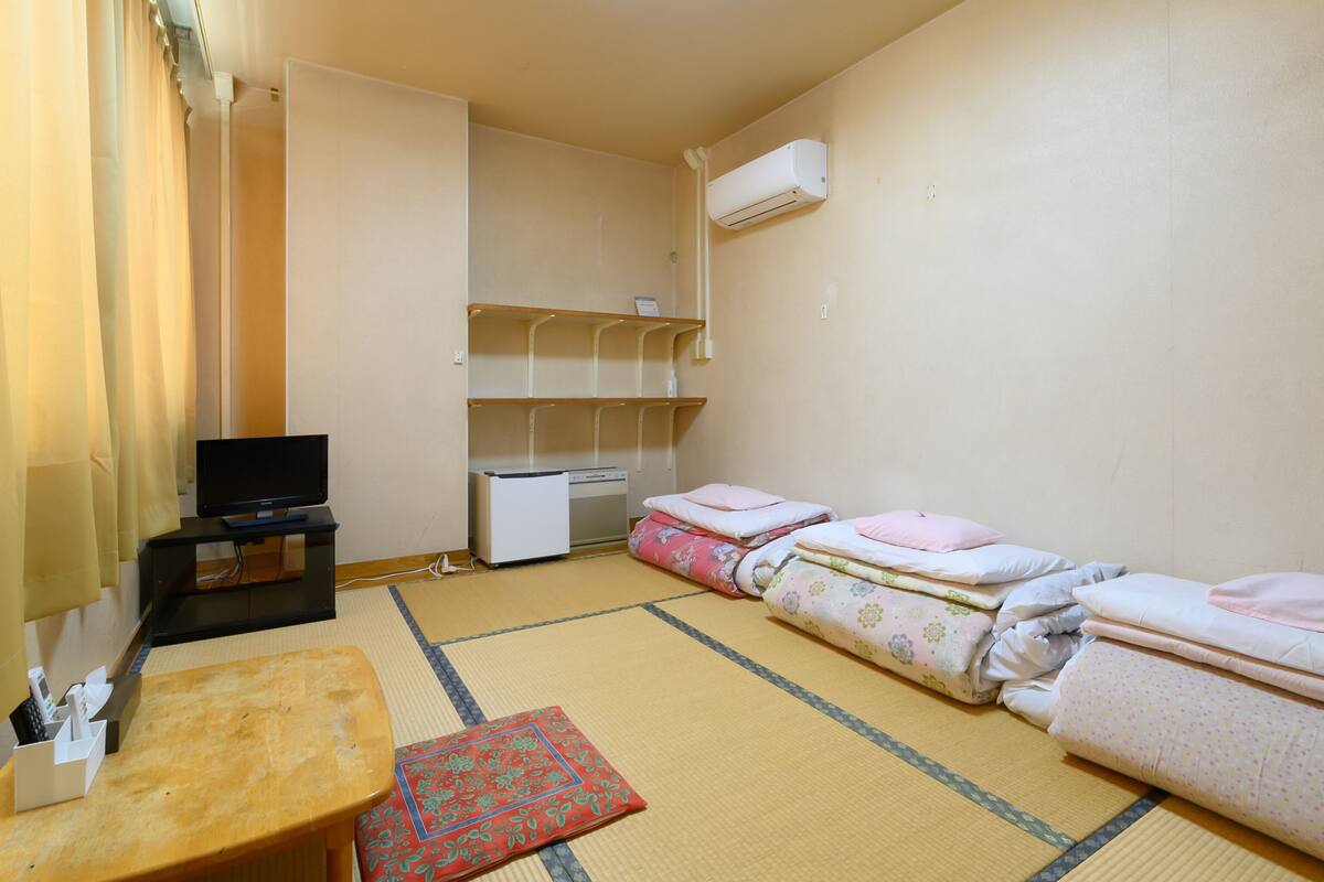 A small, tidy room with a bed, a desk, a chair, a TV, and a heater.