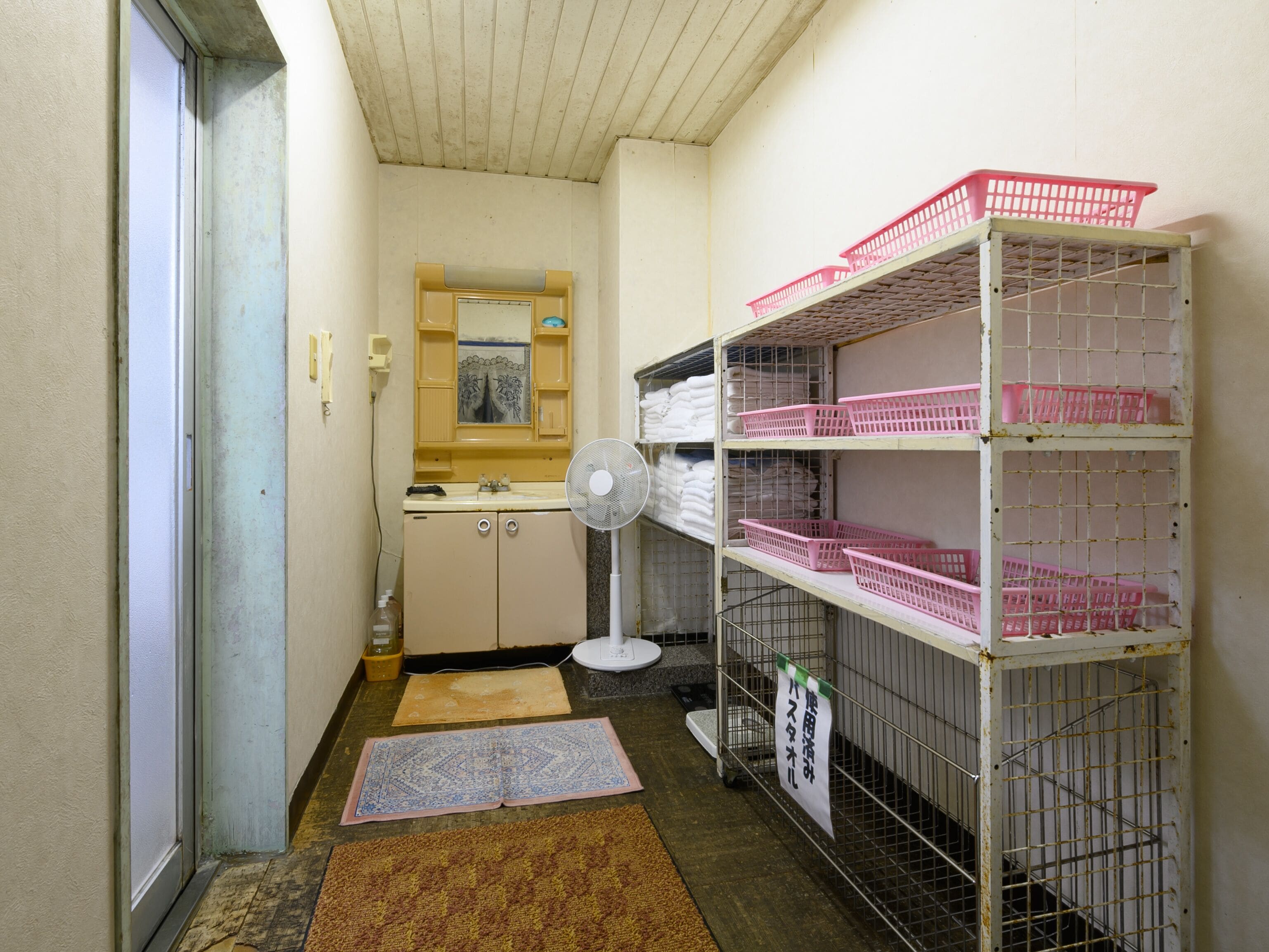A small, narrow hallway with a sink, mirror, and shelves with pink baskets.