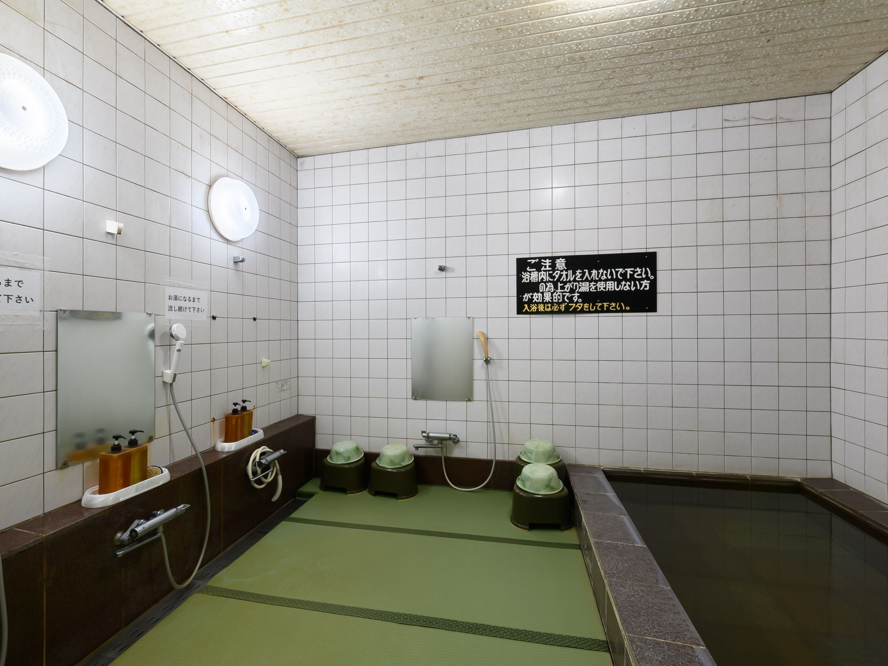 A public bath with multiple hot tubs, a green mat, and a sign with instructions.