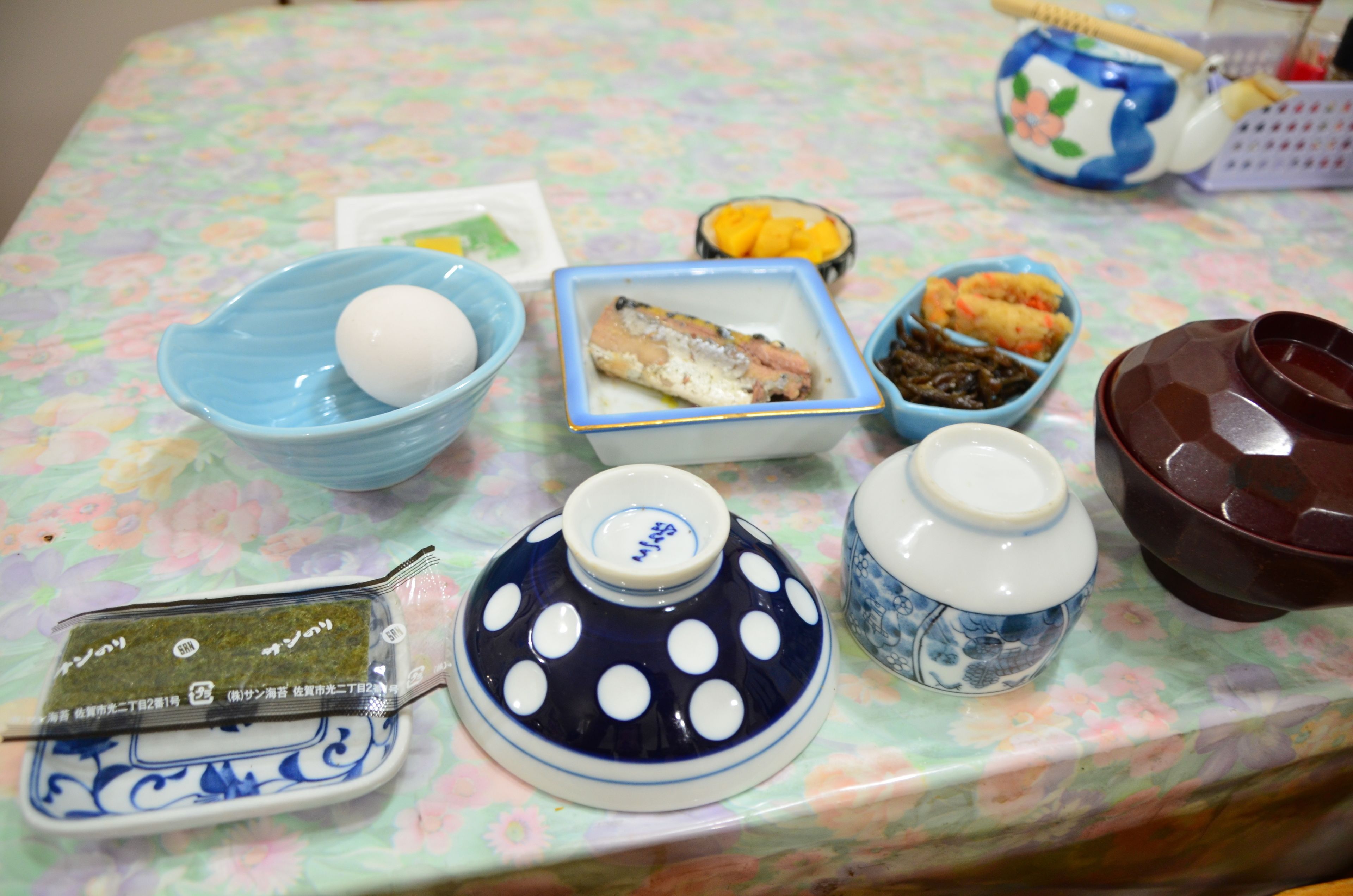 Uma mesa com diversos pratos e recipientes, incluindo uma tigela azul com um ovo, um prato com peixe e uma pequena tigela com uma fruta amarela.
