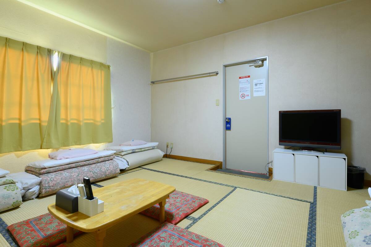 A hotel room with tatami mats, a futon bed, a wooden table, a television, and a cabinet.