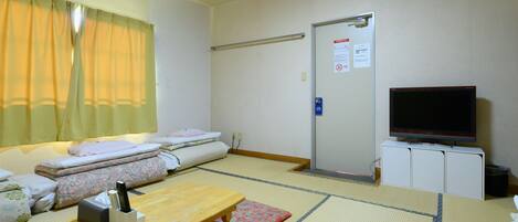 A hotel room with tatami mats, a futon bed, a wooden table, a television, and a cabinet.