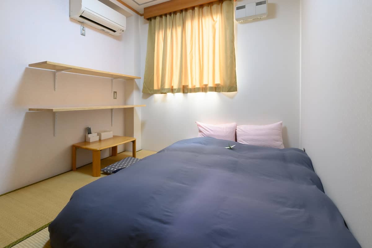 A bedroom with a bed, a shelf unit, a bedside table, and an air conditioning unit.