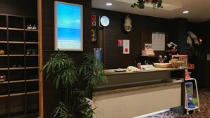 A hotel reception area with a digital clock, a reception desk, a shoe rack, and potted plants. - Tabist Yuen no yado Fujimi (Fuji)