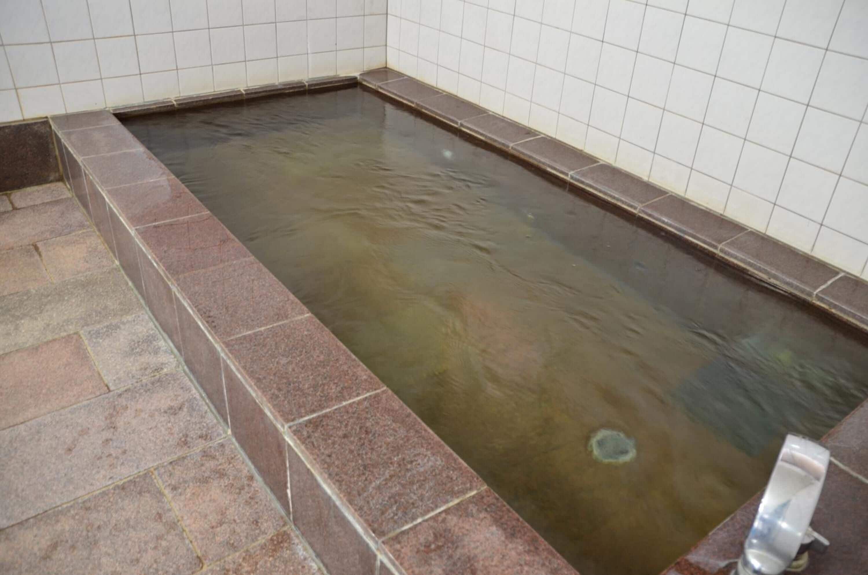 A rectangular hot tub with a tiled interior and a stone border.