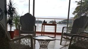 Een balkon met rieten stoelen en een klein tafeltje, met uitzicht op een waterpartij en een brug.