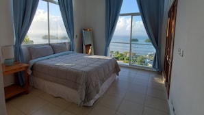 Een slaapkamer met een bed, nachtkastje, spiegel en uitzicht op zee.