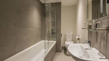 Een moderne badkamer met een douchecabine van glas, een witte badkuip, een wastafel en een toilet.