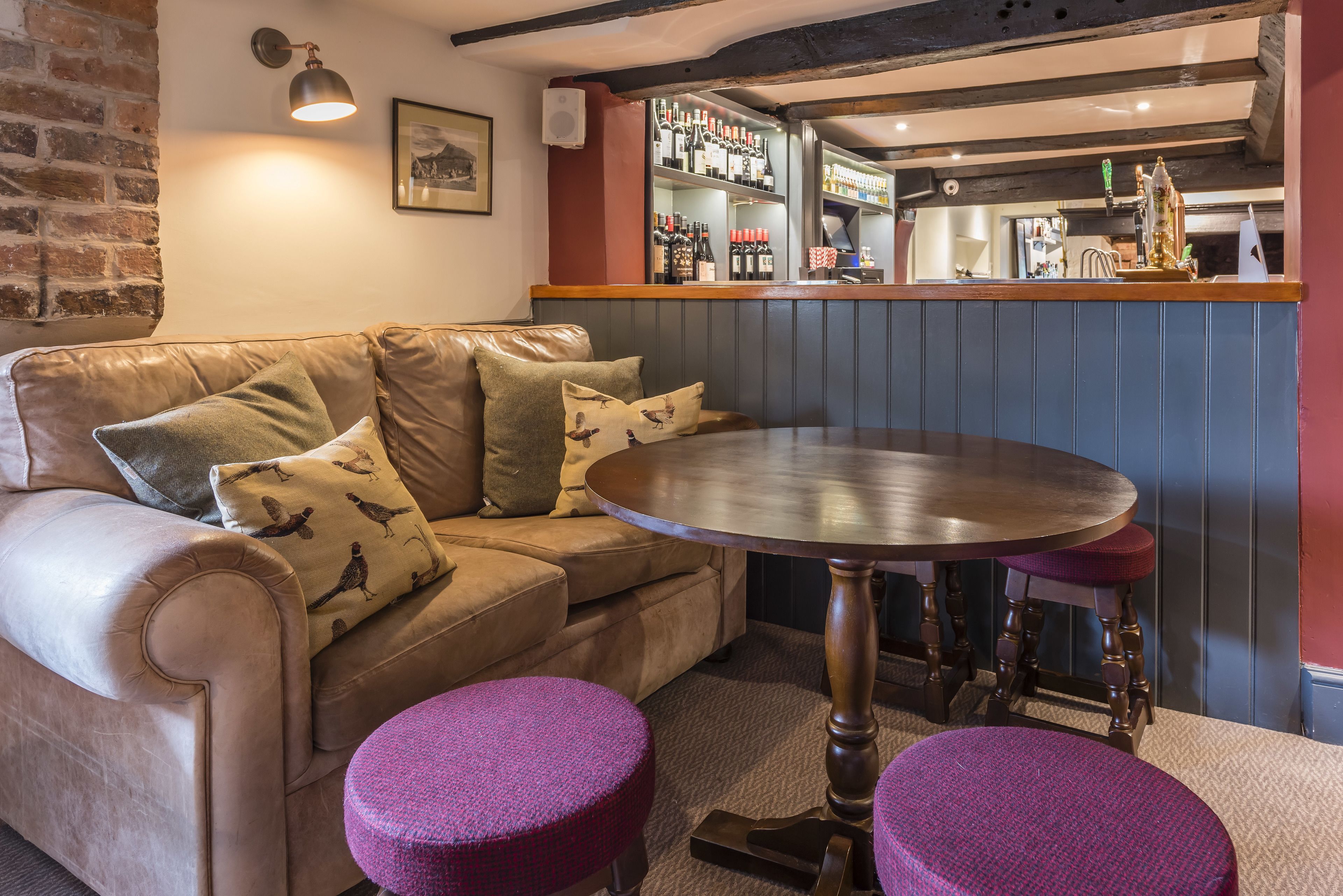 A cozy room with a leather sofa, two purple ottomans, a round table, and a bar area with shelves of bottles.