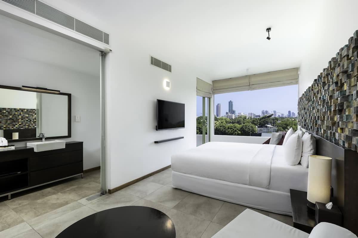 A modern hotel room with a large bed, a flat-screen TV, a bathroom with a sink and mirror, and a city view.