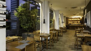 A restaurant with wooden tables and chairs, a bar area, and large windows overlooking greenery. - ME Colombo (Colombo)