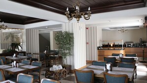 Un restaurante con mesas y sillas de madera, una araña y una zona de bar.