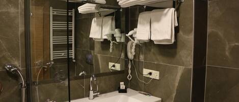 A modern bathroom with a glass-enclosed shower, a white sink, and a towel rack with multiple towels.