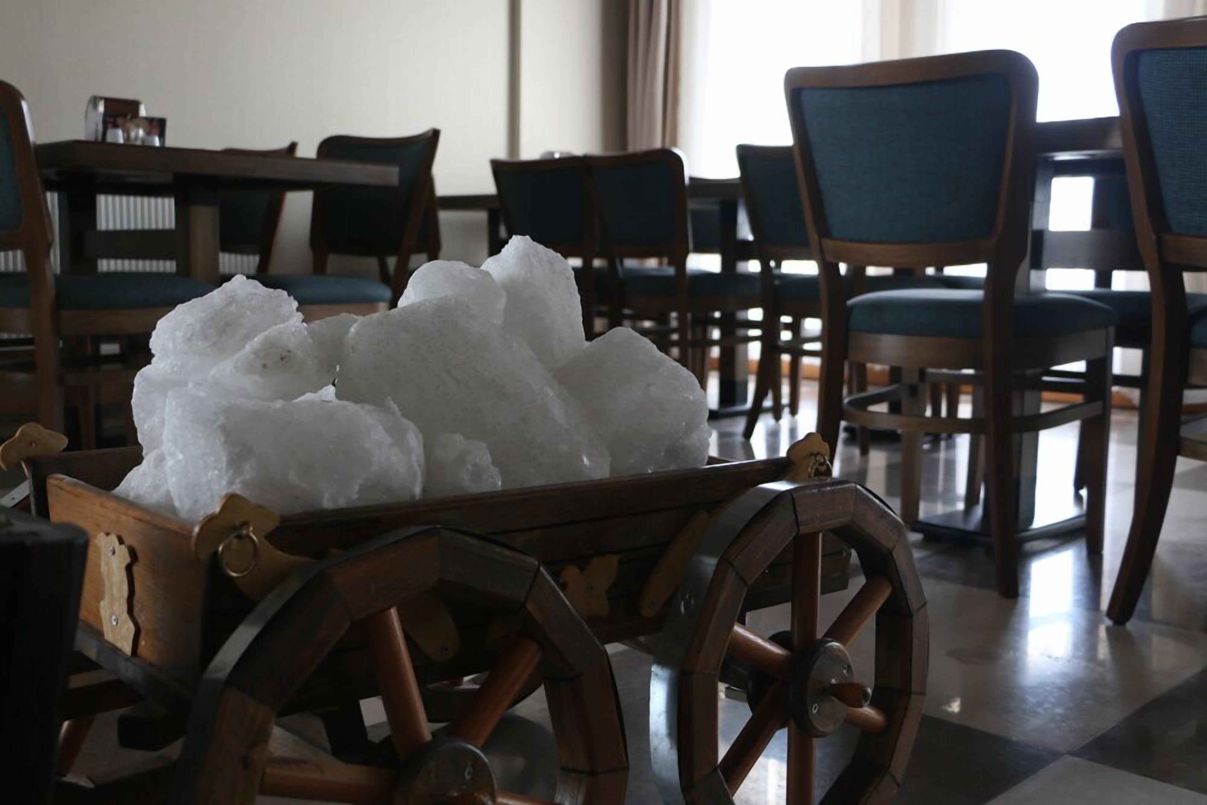 A wooden cart filled with ice in a room with wooden chairs and tables.