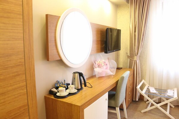 A hotel room with a wooden desk, a flat-screen TV, a round mirror, a small table with a kettle, cups, and a bouquet of flowers. - Akbak Otel (Ilgaz)