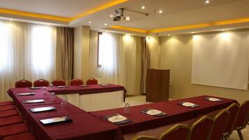 A conference room with a long table, red chairs, a podium, and a projector screen.